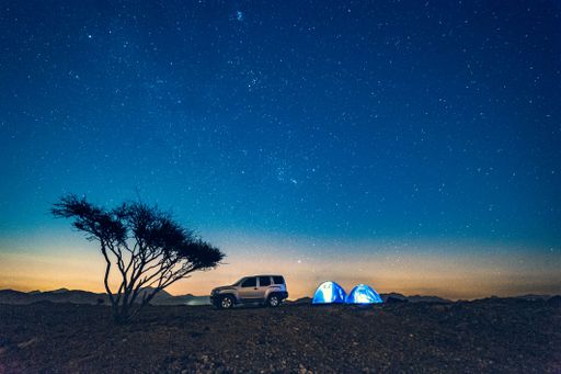 An off-road car and tents on a hill under a starry night