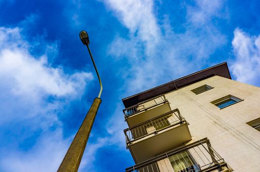 A low angle shot of a simple apartment building and a street lamp under a blue sky covered with clouds