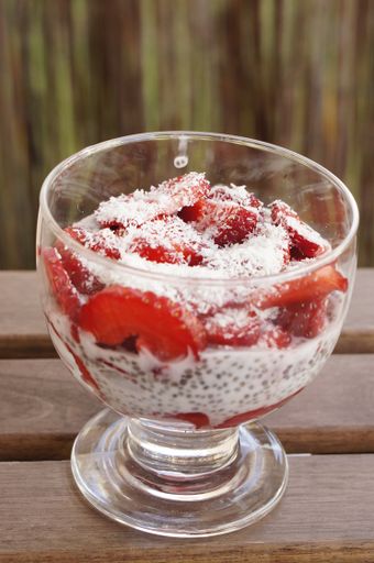 A closeup shot of a tasty, fresh and healthy strawberry yogurt with grated coconut poured on it in a glass jar put on a wooden table