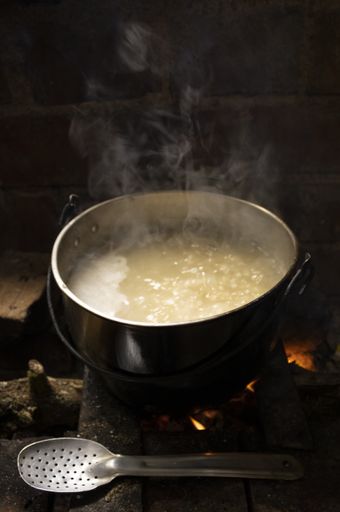 A vertical shot of an old pot standing on wood burning stove with steam from cooking