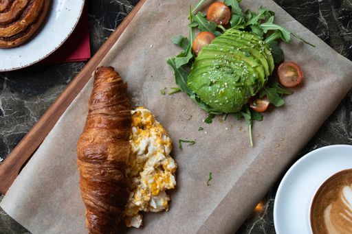 A high angle shot of a fresh croissant with eggs and avocadoes on a parchment paper