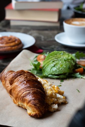 A vertical shot of a croissant with eggs and fresh avocadoes on a parchment paper