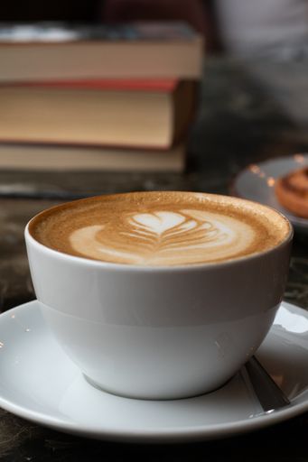 A vertical closeup shot of a cup of Latte coffee near some books on a table