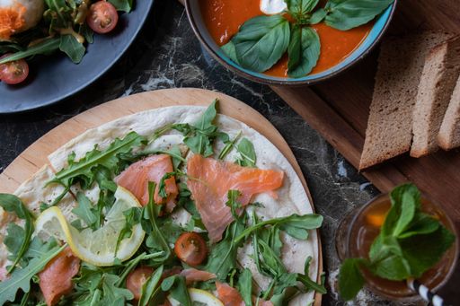 A high angle shot of sliced salmon with arugula tomatoes and lemon on a flatbread and a glass of juice