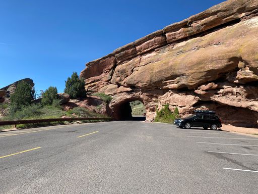 A black car parked near a huge rock tunnel in Red Rocks Park, Colorado
