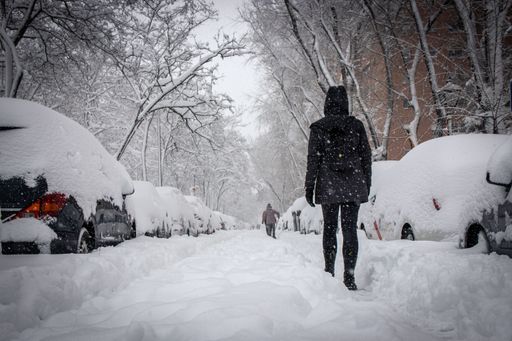 A back view of people walking on snowy street between snow-covered vehicles