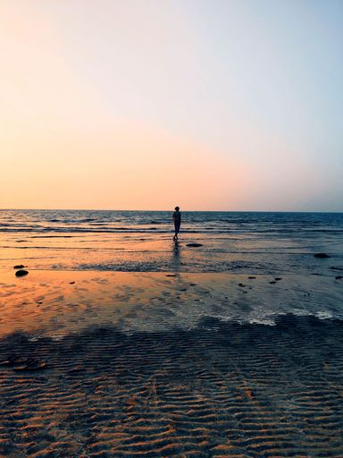 A vertical distant view of a young female walking at the coast of an ocean during sunset