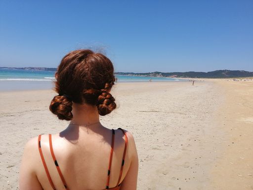 A back view of a young Caucasian female standing on a sandy beach at daytime