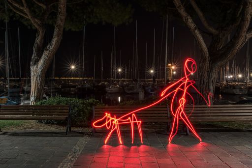 A light effect of a person walking a dog with steel wool effect in the park in Italy at nighttime