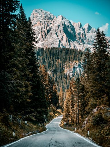 A scenic view of the winding road through the autumn forest to the majestic mountains in Dolomites, Italy