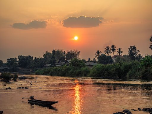A scenic view during sunset of a tropical village where the orange sun is reflected in the lake