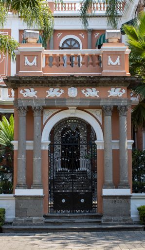A vertical shot of an archway entrance gate of a mansion with palm trees in the background