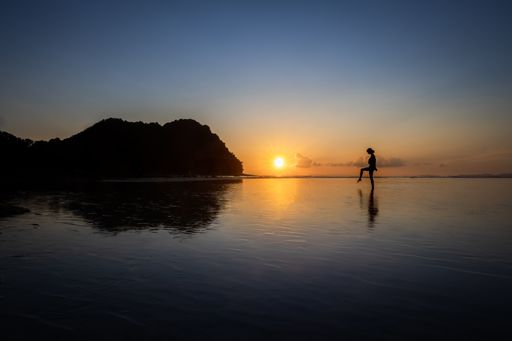 A silhouette of a female dancing on the water with the sun shining in a blue sky in the background. great for blog or background