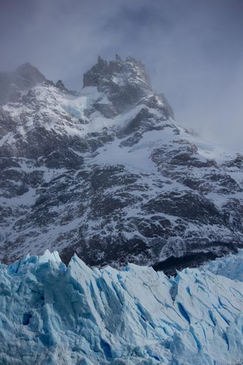 A vertical low angle shot of snow-covered mountain against the cloudy sky