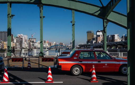 A closeup of a red taxi crossing over a green bridge behind red traffic cones in Tokyo Japan