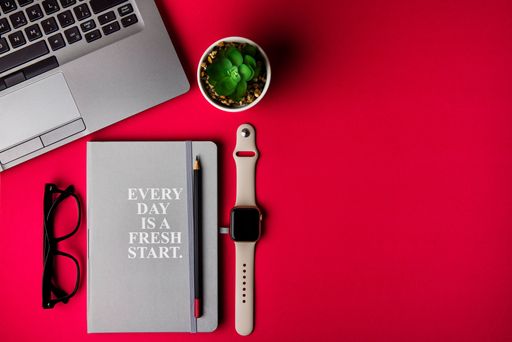 A flat lay office desk with laptop, notebook, smartwatches, and office staff