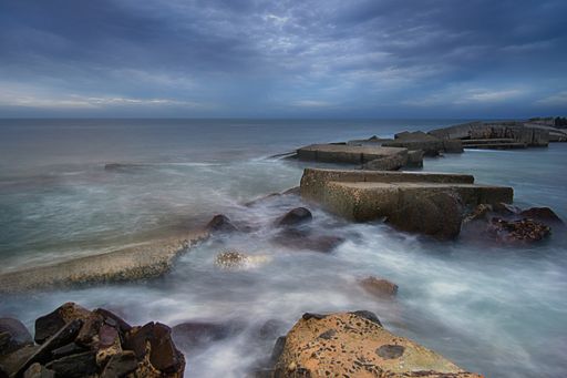 A beautiful shot of ocean waves crashing on rocks under a cloudy sky