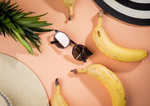 An overhead shot of sunglasses surrounded by beach hats banana and pineapple -tropical vacation concept