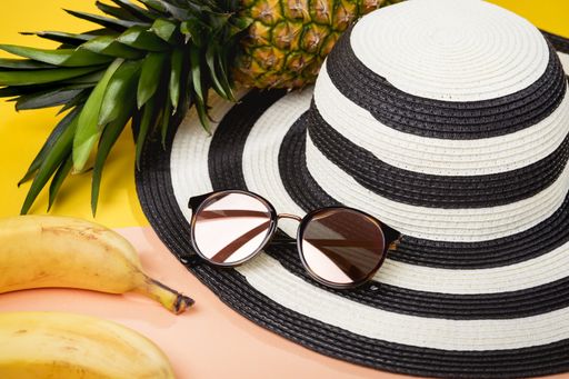 An overhead shot of sunglasses surrounded by beach hat banana and pineapple -tropical vacation concept