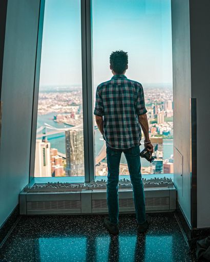 A young man standing with a camera and looking out of a window at One World Observatory