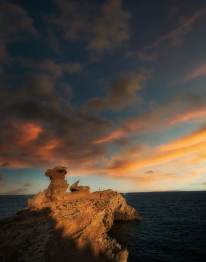 A vertical shot of a rocky island under cloudy sky