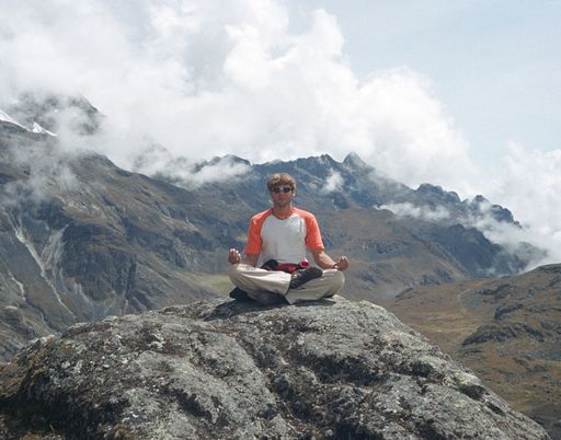 A young male in sunglasses practicing yoga in the mountains