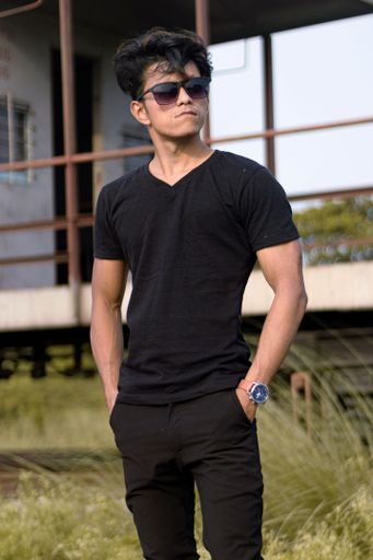 A vertical shot of an attractive East Asian man in a black outfit standing the hands in the pockets