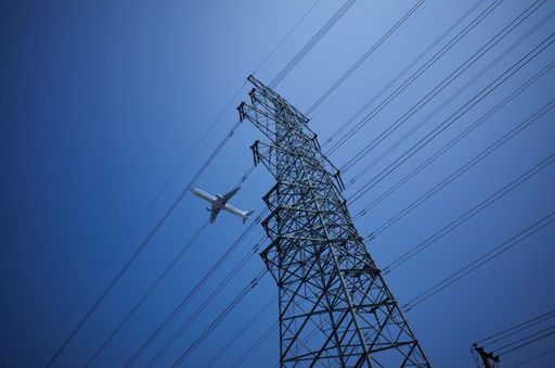 A low angle shot of an airplane flying above the electric power transmission lines against a blue sky
