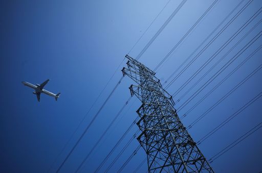 A low angle shot of an airplane flying above the electric power transmission lines against a blue sky