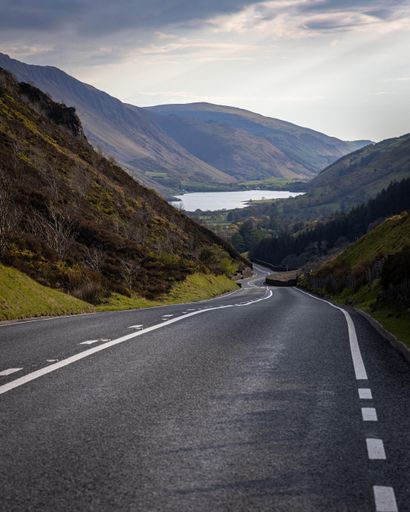 A vertical shot of a welsh road asphalt highway between green hills and dramatic sky