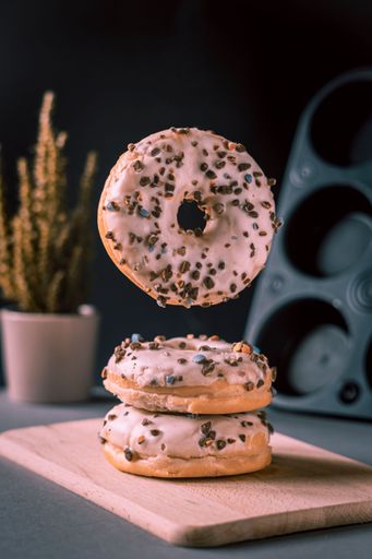 A closeup of pink donuts on the wooden board, against a cactus and form for cooking, a vertical shot