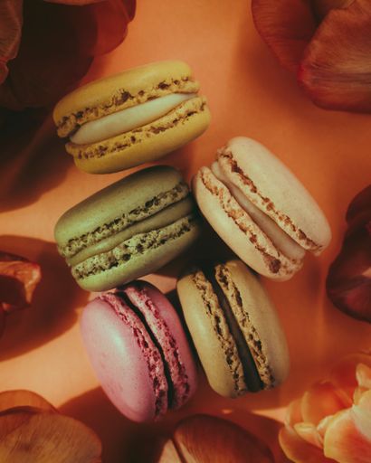 A top view of colorful macarons surrounded by tulip petals, a vertical, closeup shot