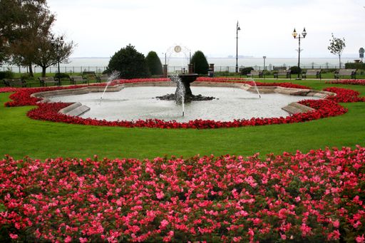 A fountain in a garden surrounded by red and pink azaleas
