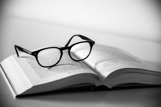 A grayscale shot of a pair of glasses on an open book with a white background