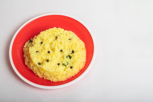 A closeup of homemade Ven Pongal dish on a red plate against a white surface
