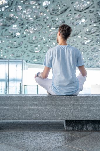 A vertical shot of a young male sitting cross-legged on a stone