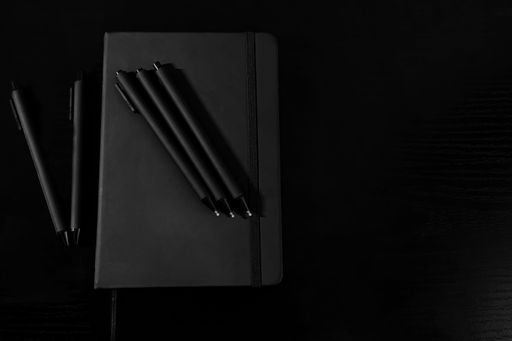 A notebook and pens on black background