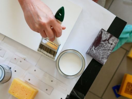 A top view of painting tools and hand holding a brush and painting something on the white surface