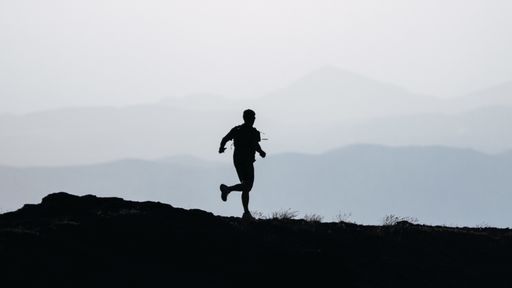 A greyscale shot of the silhouette of a person running on a hill