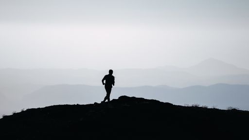 A greyscale shot of the silhouette of a person running on a hill