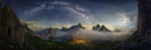 A beautiful panoramic shot of a mountain valley with a small illuminated house under the starry sky