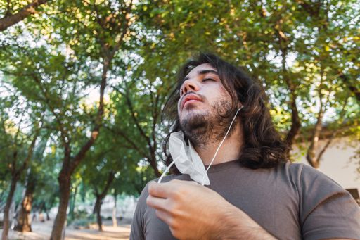A low angle shot of a young European man enjoying a breath of fresh air after removing face mask under lush trees