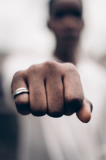 A vertical closeup of an Afro American guy's fist on a blurry background with a ring on his pinky