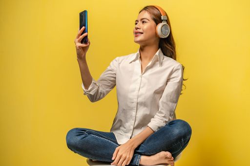 An Asian woman looking at her phone and listening music in yellow background