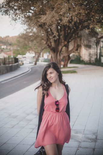 A young beautiful Latin female wearing a cute coral dress standing on the street