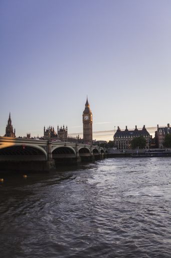 A vertical shot of the Big Ben tower behind the river Thames in London