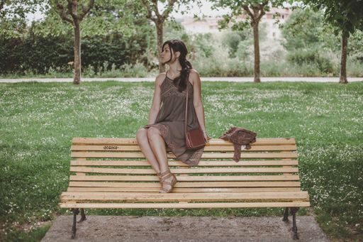 A Caucasian female in a dress sitting on a wooden bench in a park in Spain