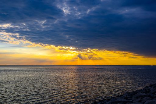 A scenic view of sun rays piercing through the clouds over the sea during sunset
