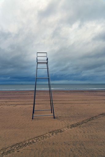A vertical shot of an empty lifeguard chair on a beach shore with a cloudy sky in the background