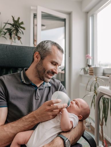 A vertical shot of a Caucasian dad feeding his baby with a bottle of baby formula.